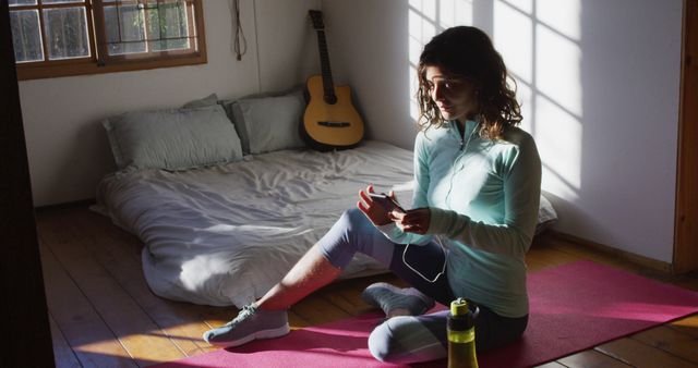 Happy biracial woman preparing for workout, using smartphone sitting on floor in sunny bedroom - Download Free Stock Photos Pikwizard.com