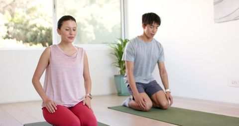 Young couple practicing kneeling yoga and mindfulness in bright studio with green mats