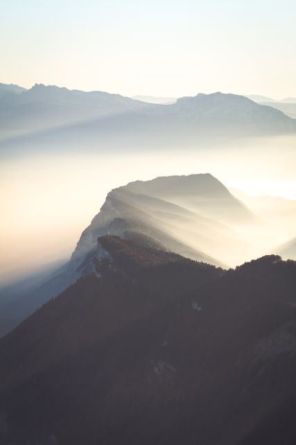This image captures the serene beauty of misty mountain ridges bathed in the soft light of sunrise. The beams of sunlight cutting through the mist evoke a sense of tranquility and natural wonder. Ideal for use in travel magazines, nature blogs, inspirational posters, and environmental campaigns, this image can convey themes of peace, beauty, and the awe-inspiring majesty of nature.