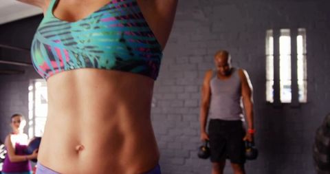 Toned woman torso stretching in industrial gym while teammates lifting kettlebells