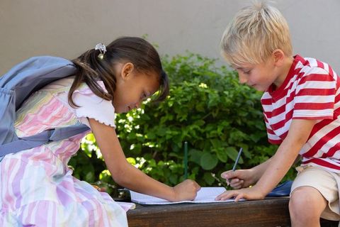 Children collaborating on homework outdoors on school bench, writing together