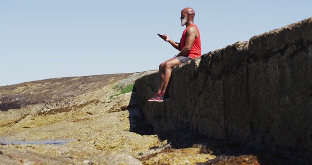 Elderly Man Relaxing on Coastal Wall with Smartphone on Sunny Day - Download Free Stock Images Pikwizard.com