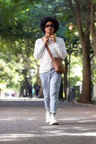 African american man walking through tree-lined park wearing casual crossbody bag