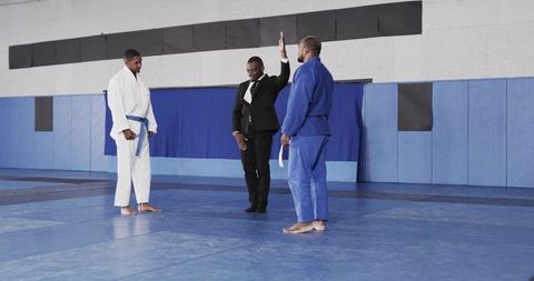 Diverse martial arts competitors instructed by referee in dojo