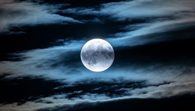 Glowing Full Moon Hovering in Night Sky, Wispy Clouds Revealing Cratered Lunar Surface