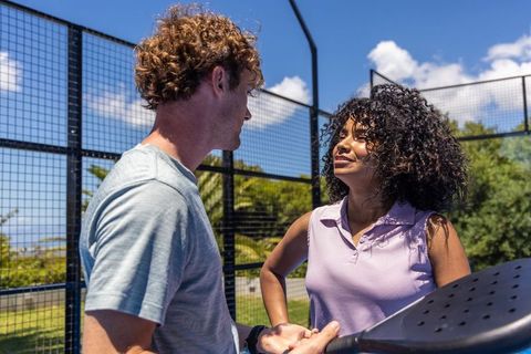 Playing paddle outdoors on sunny fenced court, young couple sharing friendly competition