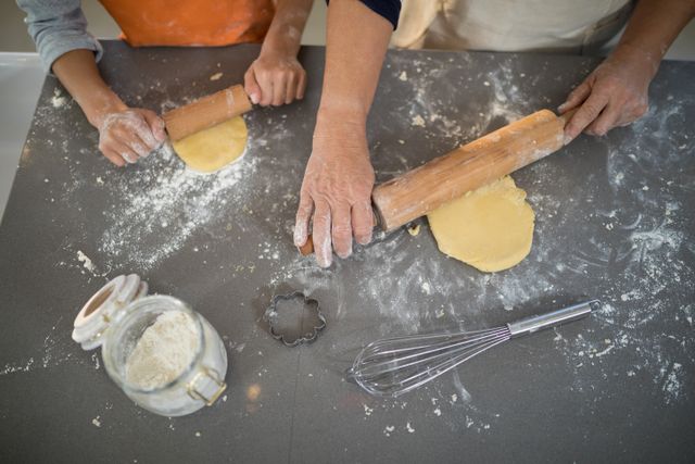 Close-up of grandmother and granddaughter flattening dough in the kitchen
