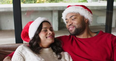 Couple wearing santa hats cuddling on couch sharing warm smiles cozy holiday romance