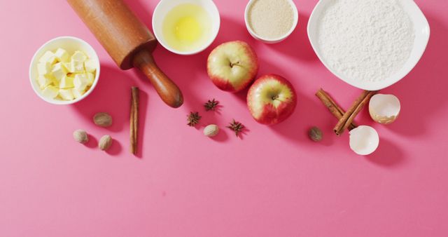 Perfect for food blogs, recipe books, and kitchen decor. Showcases key ingredients for making apple pie including butter, flour, eggs, apples, and spices. Contains rolling pin suggestive of action-oriented preparation. Bright pink background adds color contrast, making ingredients pop.