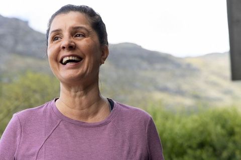 Mature woman laughing on porch overlooking hills wearing purple active top