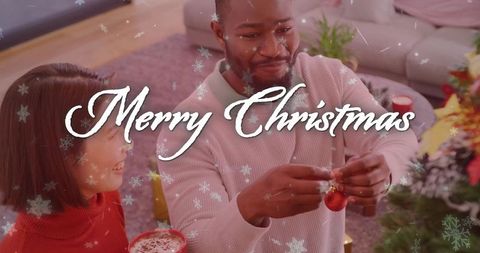 Couple decorating christmas tree together with red bauble and cozy hot cocoa