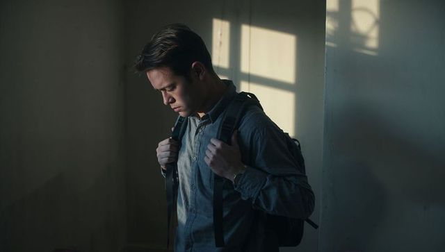 Solitary Asian man standing with backpack in moody sunlight, contemplative portrait