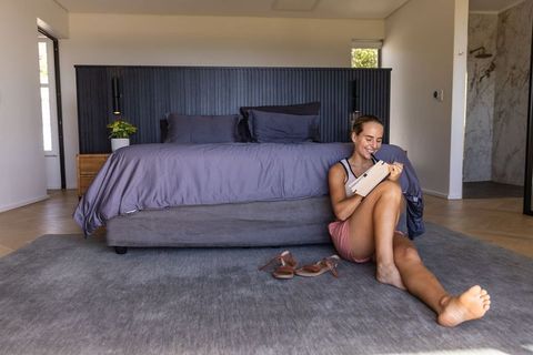 Woman reading tablet on bedroom floor during relaxed morning in minimalist bedroom