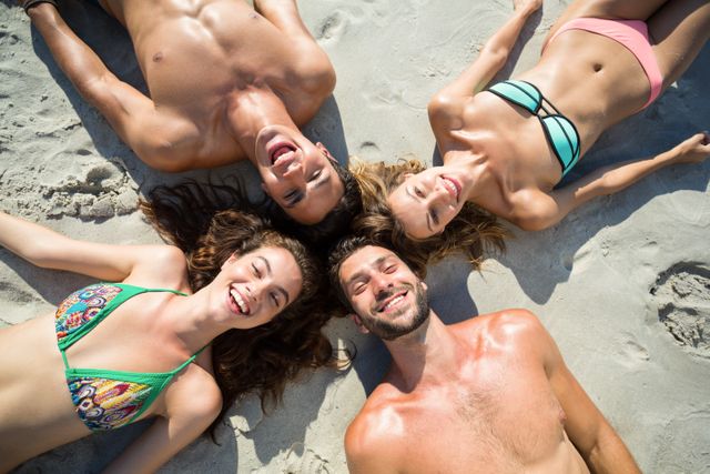 Group of friends lying on sandy beach, smiling and enjoying sunny day. Perfect for promoting summer vacations, beachwear, outdoor activities, and friendship. Ideal for travel brochures, lifestyle blogs, and social media campaigns.