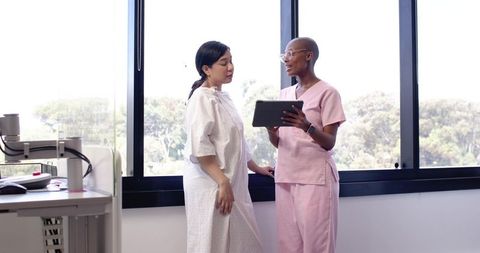 Nurse Reviewing Tablet while Discussing Results with Patient by Window in Clinic