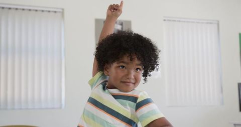 African american preschool boy raising hand in bright classroom, joyful learning moment