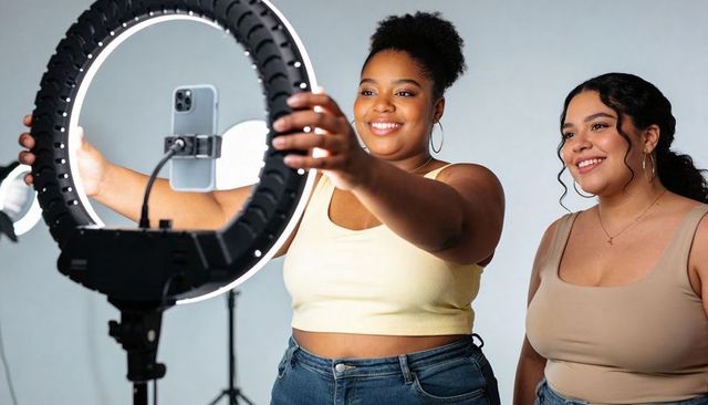 Two female creators adjusting led ring light recording social media content together