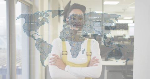 Confident businesswoman standing with arms crossed in yellow overalls behind digital world map