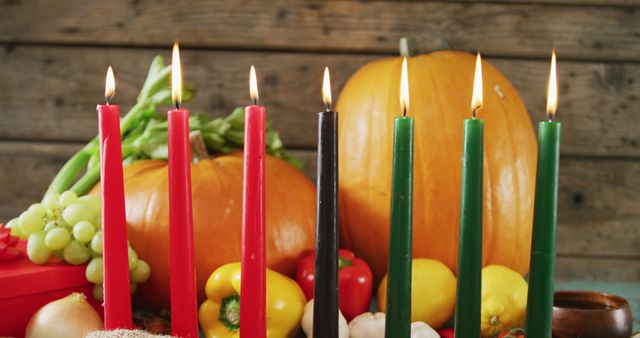 Depicts Kwanzaa candles lit with vegetables and pumpkins arranged on a wooden table, representing a festive atmosphere. Ideal for use in articles, promotional materials, and social media posts related to Kwanzaa celebrations, holiday traditions, and decorative inspiration.