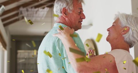 Joyful Senior Couple Dancing at Home Amidst Gold Confetti