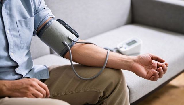 Adult man checking blood pressure on sofa using digital cuff monitor for home care