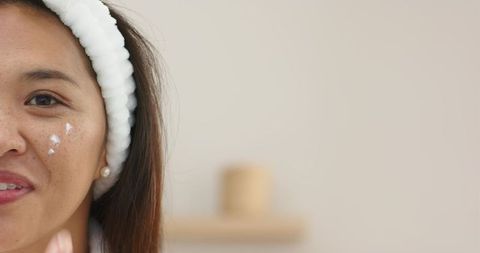 Asian Woman Smiling Applying Cream on Cheek