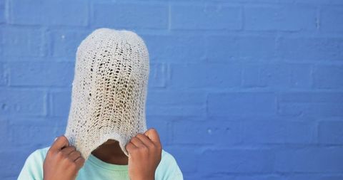 Child adjusting knitted hat against blue wall background