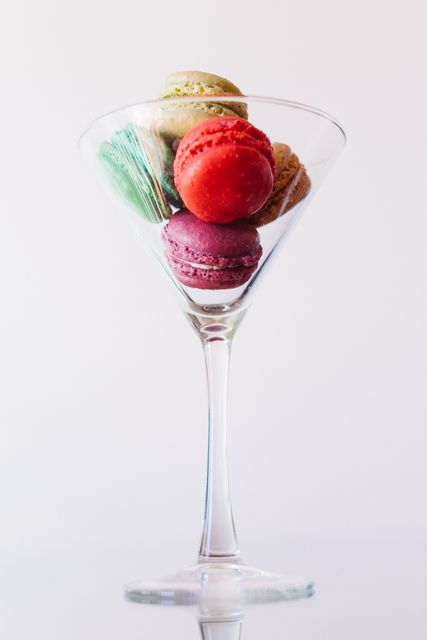 Colorful macarons neatly arranged in a martini glass create an elegant presentation against a white backdrop. Use this image for gourmet café promotions, dessert menu designs, food blogs, patisserie advertisements, or as decoration for modern culinary cookbooks. Perfect for content that highlights sophisticated indulgence and artistic food presentation.