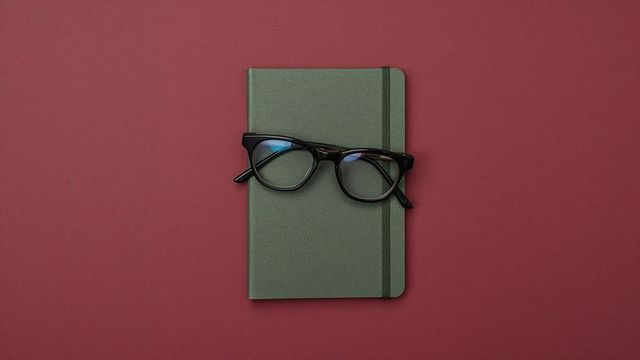 Olive Green Notebook with Eyeglasses on Burgundy Background