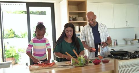 Family cooking at modern kitchen island preparing healthy salad chopping fresh vegetables