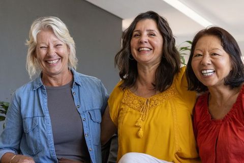 Three diverse mature women laughing together on sofa, friendship and lifestyle