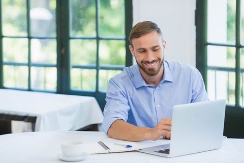 Happy Professional Man Working on Laptop at Bright Café
