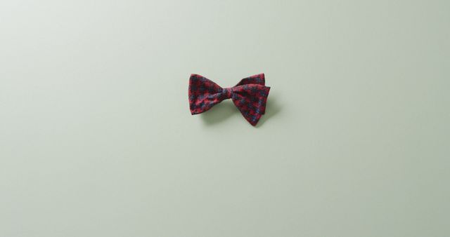 Red tartan bow tie on light green background, ideal for use in promotions related to men's fashion, formal wear, or accessories. Suitable for websites, online stores, advertisements, or design elements in flyers and posters.