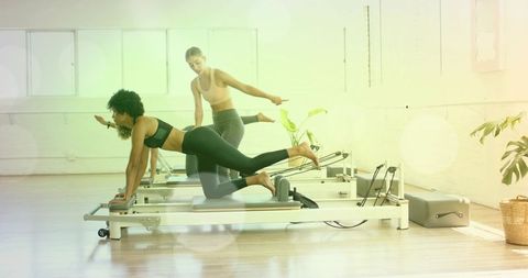 Pilates reformer class with instructor guiding leg extension in bright sunlit studio