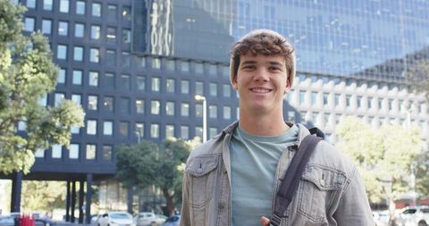 Smiling college student with backpack on sunny downtown street by modern office building