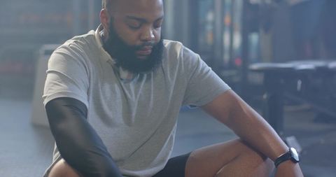 African american athlete resting on gym floor wearing compression sleeve and headphones