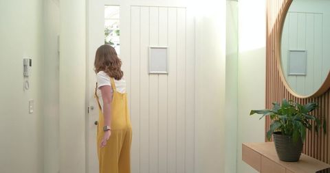 Woman standing back-turned reaching doorknob in bright modern minimalist foyer