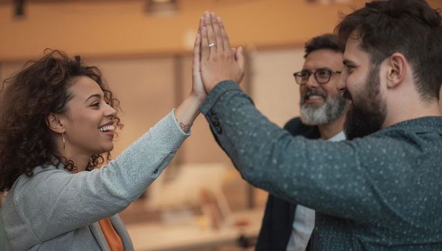 Team celebrating success with high five in open office showcasing collaboration and unity