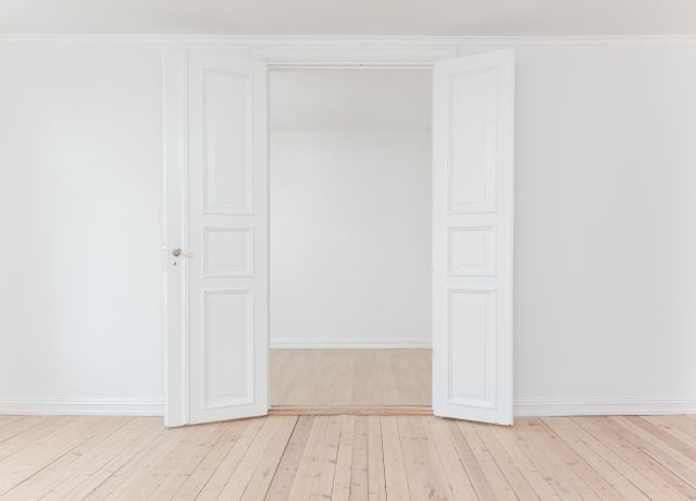 This image captures a spacious, minimalist interior with white double doors opening into an empty room with wooden flooring. Perfect for real estate listings, interior design projects, home decor blogs, or promotional materials for minimalist home designs.