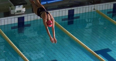 Competitive swimmer diving from starting block into pool wearing pink cap and goggles