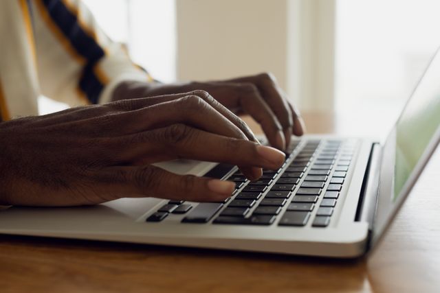 This image captures the hands of an African-American man typing on a laptop, emphasizing the use of technology in a professional or home office setting. Ideal for illustrating concepts related to remote work, digital communication, business tasks, and modern technology use in various professional contexts.