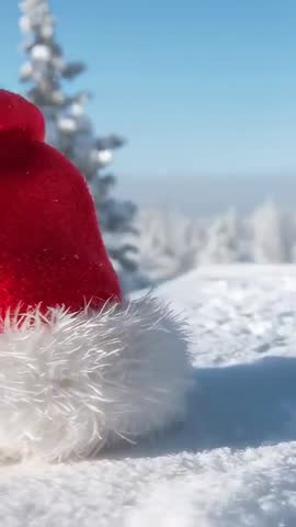 Vertical video panning over red Santa hat resting on snowy ledge with falling snowflakes