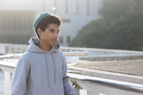 Contemplative backlit african american teen standing on rooftop wearing gray hoodie and green beanie