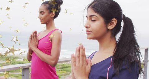 Coastal morning meditation duo practicing prayer pose on balcony overlooking ocean