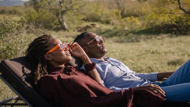 Couple lounging in meadow wearing orange sunglasses enjoying sunlit outdoor relaxation