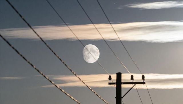 Full moon framed by power lines at dusk with silhouetted utility pole and streaked clouds