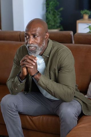 Contemplative senior african american man clasping hands, looking left on couch