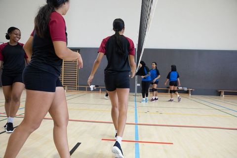Teen female volleyball players walking across gym toward net during school practice session