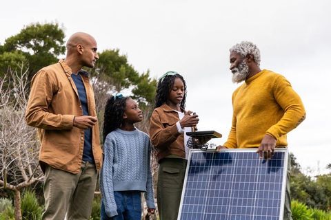 Grandfather mentoring family installing backyard solar panel, teen learning renewable energy