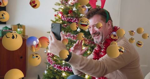 Mature man recording christmas selfie with ar emojis wearing reindeer antlers and tinsel